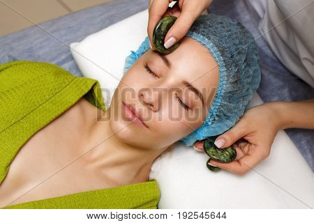 Spa treatment. Facial massage with jade stones. Alternative medicine. Massage the forehead area. Guasha