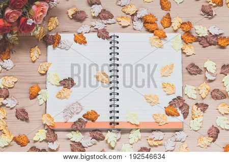 Spiral notebook with rose and maple leaves on wood background in autumn