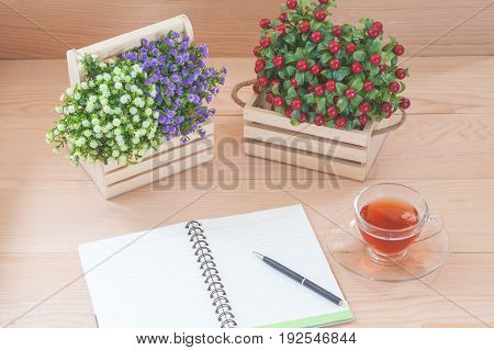 Spiral notebook with tea and flowers on wood background