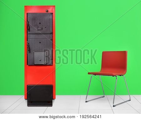 Energy savings concept. Solid fuel boiler and chair on color wall background