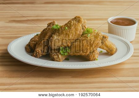 Fried chicken wings on white plate served with barbecue dipping sauce. Homemade fried chicken delicious and crispy. Thai style fried chicken and chili sauce or tomato sauce (ketchup) ready to served. Deep fried chicken wings. Street food.