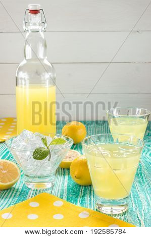 lemonade or limoncello in a yoke stopper bottle drink in glasses sherbet glass with ice cubes decorated by mint leaf on turquoise colored wooden table with yellow napkin at white polka dots.