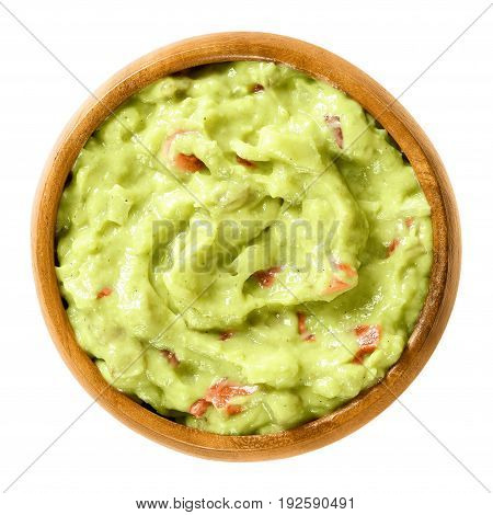 Guacamole in wooden bowl. Also short guac, a light green dip or salad, made of mashed avocados, tomatoes, onions, garlic, lemon, cayenne pepper and salt. Macro food photo close up on white background.