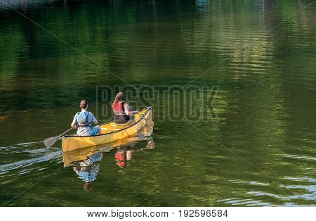 Male and female caucasian couple paddling a yellow canoe on a very calm morning on tree lined lake
