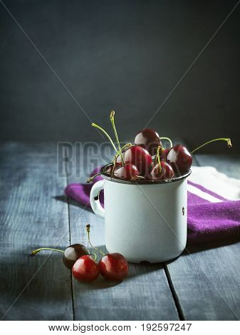 Ripe cherries in an iron mug on a dark blue wooden background. With copy space.