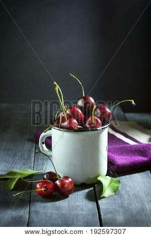 Ripe cherries in an iron mug on a dark blue wooden background. With copy space.