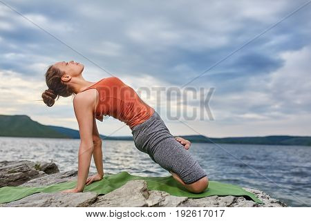 Young sporty woman doing different variants of yoga position on a rocky rivershore. Beauty woman dressed in the sportwear and barefoot. Beautiful landscape like a background. Concept of the healthy and active lifestyle.