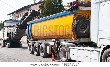 Road construction asphalt paving of a road. Dumper truck is loaded with asphalt milled from cold planer machine.