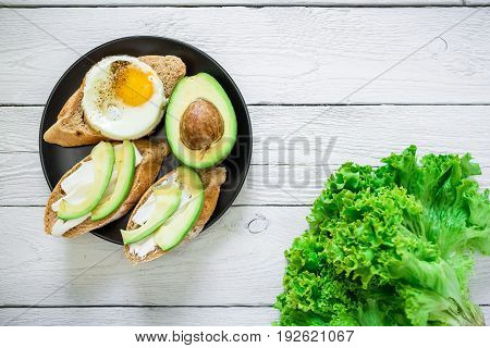 Tasty sandwiches with avocado and egg on plate on white wooden table. Delicious breakfast. Flat lay/ Top view