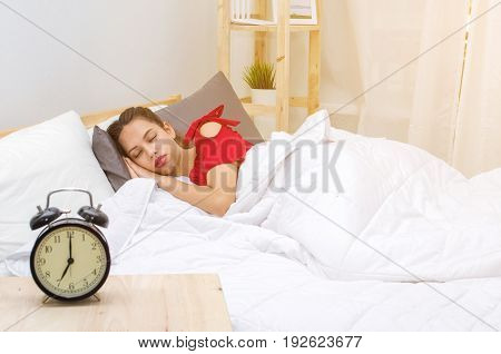A asian young woman in red pajamas sleeping on bed and alarm clock in bedroom at the morning selective focussunlight effect