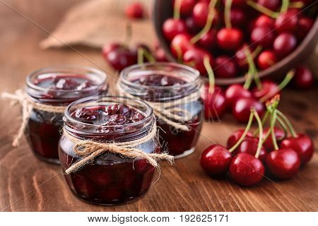Cherry jam on wooden background in glass jars