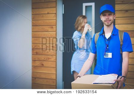Smiling delivery man in blue uniform delivering parcel box to recipient - courier service concept