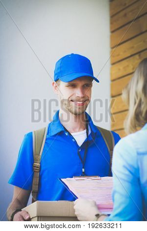 Smiling delivery man in blue uniform delivering parcel box to recipient - courier service concept