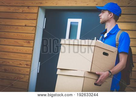 Smiling delivery man in blue uniform delivering parcel box to recipient - courier service concept