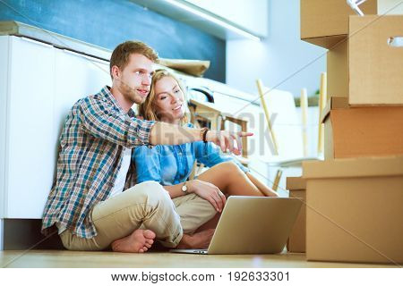 Young couple moving in new home.Sitting on floor and relaxing after unpacking.Looking something on laptop