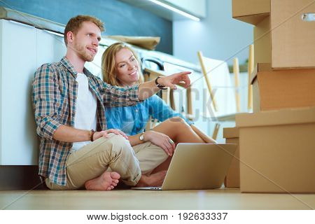 Young couple moving in new home.Sitting on floor and relaxing after unpacking.Looking something on laptop