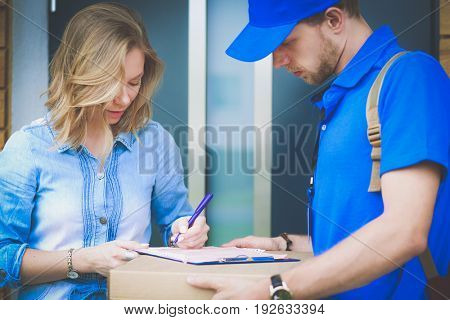 Smiling delivery man in blue uniform delivering parcel box to recipient - courier service concept