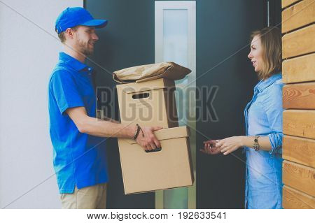 Smiling delivery man in blue uniform delivering parcel box to recipient - courier service concept