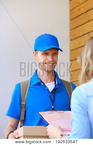 Smiling delivery man in blue uniform delivering parcel box to recipient - courier service concept