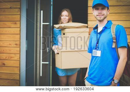 Smiling delivery man in blue uniform delivering parcel box to recipient - courier service concept