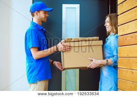 Smiling delivery man in blue uniform delivering parcel box to recipient - courier service concept