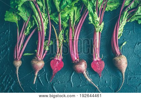 Row of homegrown organic young beets with green leaves on dark stone table. Food background. Concept of healthy eating. Toned image. Top view.
