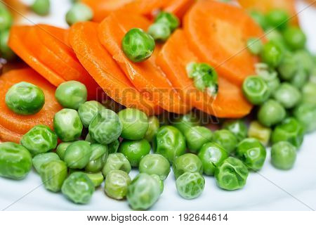 Boiled carrots and grean peas on white plate close up.