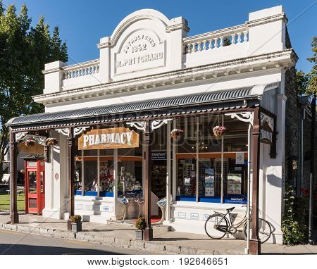 Arrowtown New Zealand - March 16 2017: The white painted old building of the active pharmacy in town. Bike and red phone booth in shot. Posters in window.