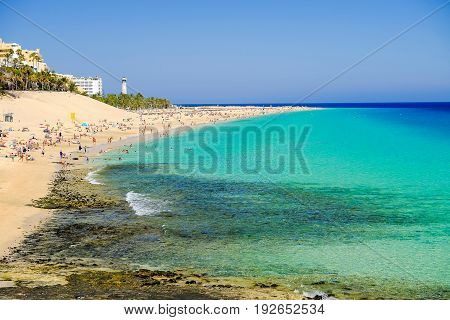 View on the beach Playa de Morro Jable in a sunny day with many people swimming in crystal water of the Atlantic ocean. Location Morro Jable on the Canary Island Fuerteventura Spain.