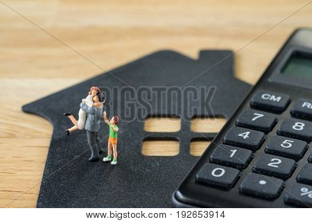 Miniature happy family figure standing on paper house with calculater as property or financial investment plan concept.