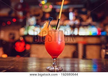 Tropical cocktail in glas garnished with orange on the bar.