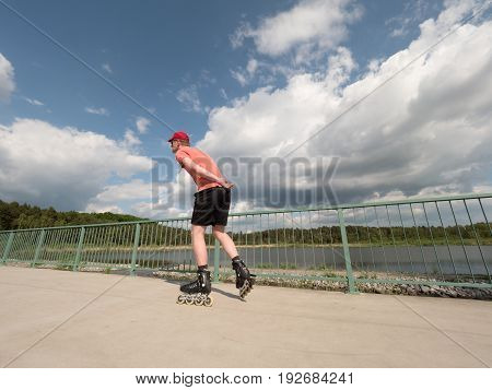 Roller Skater In Action. Man Ride In Inline Skates Ride Along Promenade Handrail, Sky In Background