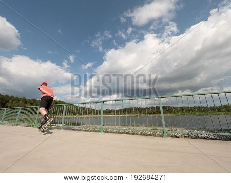 Roller Skater In Action. Man Ride In Inline Skates Ride Along Promenade Handrail, Sky In Background