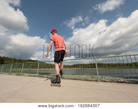 Roller Skater In Action. Man Ride In Inline Skates Ride Along Promenade Handrail, Sky In Background