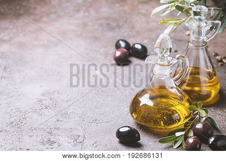 Olive oil in a glass bottle and olive branch on brown stone table