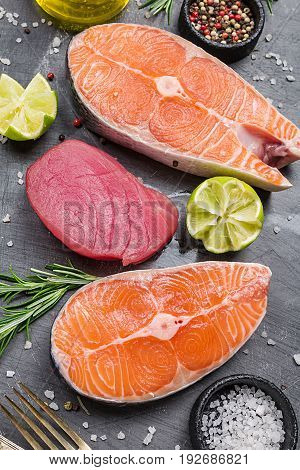 Raw tuna and salmon steak and ingredients for cooking on a dark background. Top view