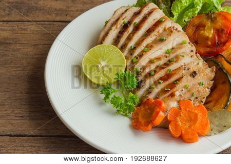 Sliced chicken breast barbecue on white plate served with grilled vegetable. Delicious chicken breast steak and salad for dinner. Homemade chicken breast barbecue on wood table for background. Chicken steak or pork chops background.