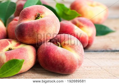 Fresh peaches with leaves on wooden background. Doughnut or vineyard type of flat peach.