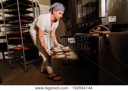 Baker taking a loaf of freshly baked bread from the oven in a modern bakery, the Baker taking fresh bread