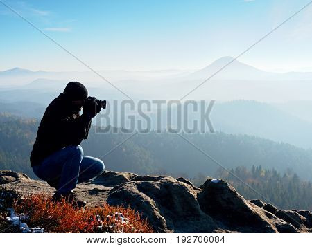 Photographer  Look Down Into Fogy Valley. Man Is Kneeling On Cliff And Takes Photos.