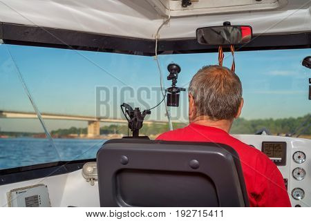 Back view of man sitting in cabin driving river boat on sunny day