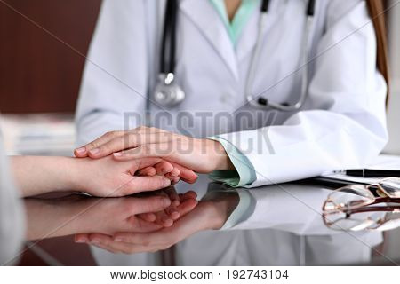 Friendly female doctor hands holding patient hand sitting at the desk for encouragement, empathy, cheering and support while medical examination. Bad news lessening, compassion, trust and ethics concept