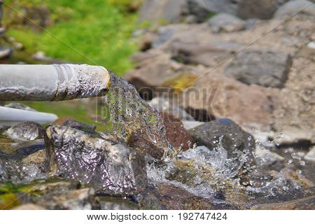 End of a rusty pipeline with a hot geothermal water flowing into the natural creek in the Icelandic natural park