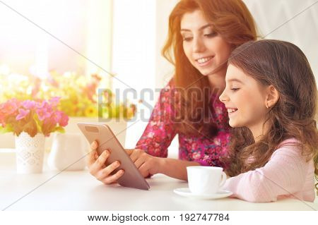Beautiful  young woman and little girl  sitting at  table and using  tablet taking selfie