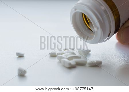 Oval pills spilling and dropped out of pill bottle on white table medicine concept
