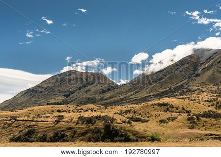 Middle Earth New Zealand - March 14 2017: Mountain range at Middle Earth under blue cloudy sky. High desert scenery with sparse brown vegetation. Shale pebble flow off top.