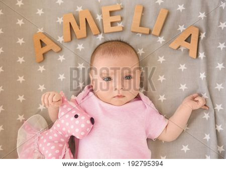 Cute baby lying on bed with toy and word AMELIA composed of wooden letters. Choosing name concept