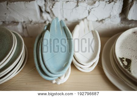 Stylish chamotte ceramic hands for rings and little things on wooden shelf with white brick wall on background in workshop