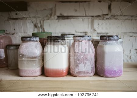 Bottles with colored glaze for ceramic on wooden shelf with white brick wall on background