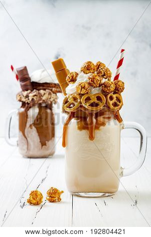 Caramel and chocolate indulgent exreme milkshakes with brezel waffles popcorn marshmallow ice cream and whipped cream. Crazy freakshake food trend.